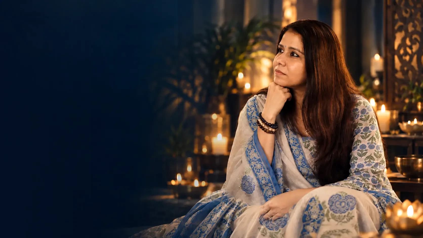 Shuchita Mitra seated in a candlelit room, gazing thoughtfully to the side